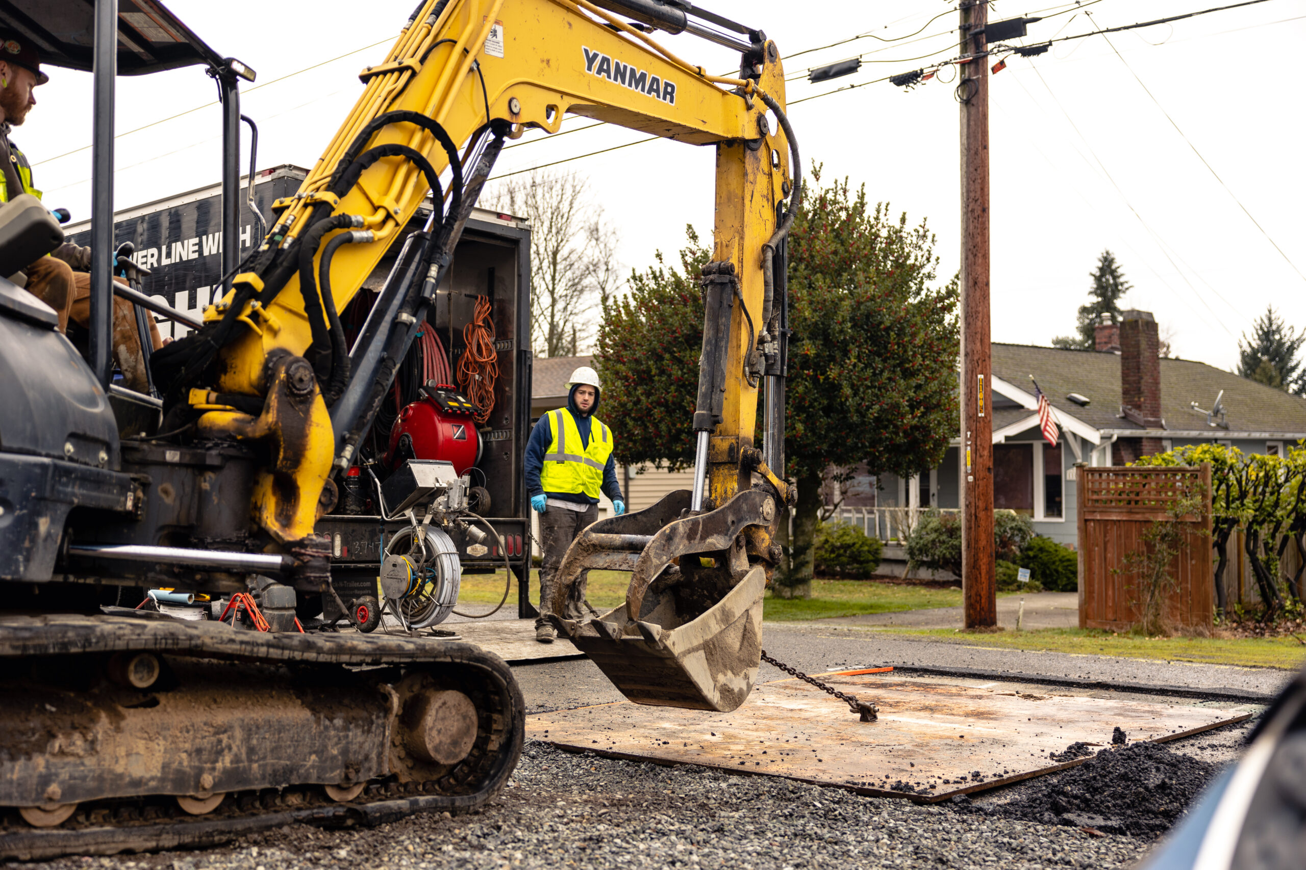 A PRICOR professional uses an excavator to break ground as a safety supervisor observes.