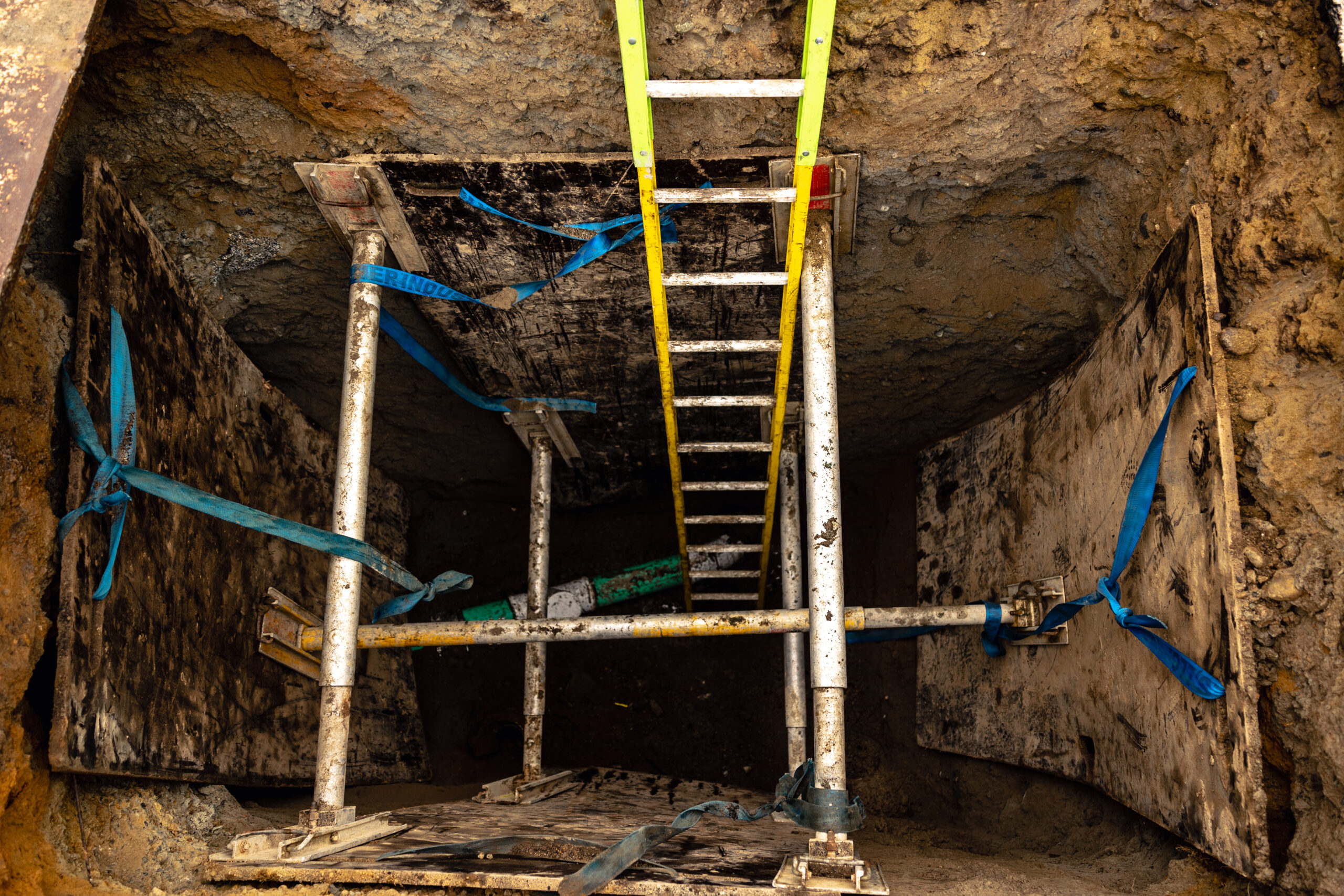 A PRICOR Technologies excavation site with a ladder descending a deep trench and vertical shores to prevent a cave-in.